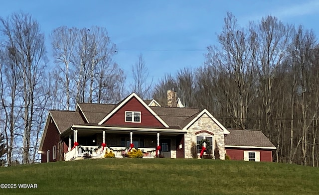 view of front of property with stone siding, covered porch, a chimney, and a front yard