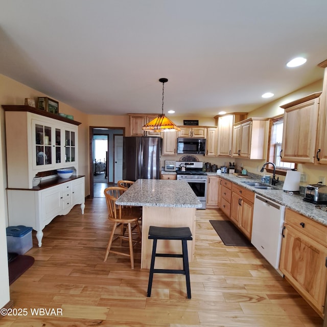 kitchen with light wood finished floors, light brown cabinets, a kitchen island, stainless steel appliances, and a sink