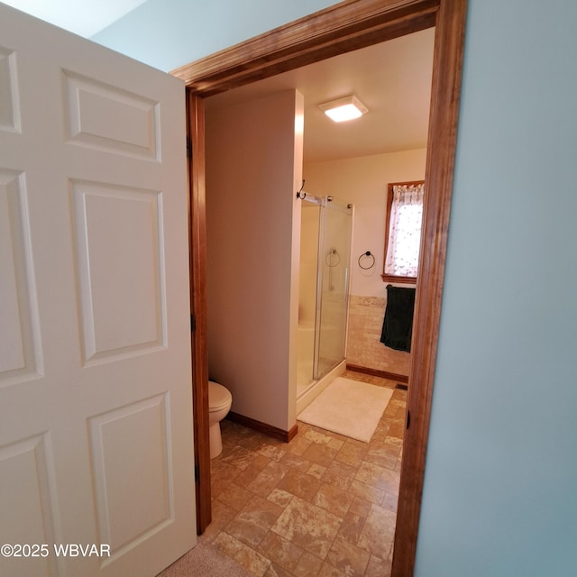 bathroom featuring a shower stall, toilet, stone finish flooring, and baseboards