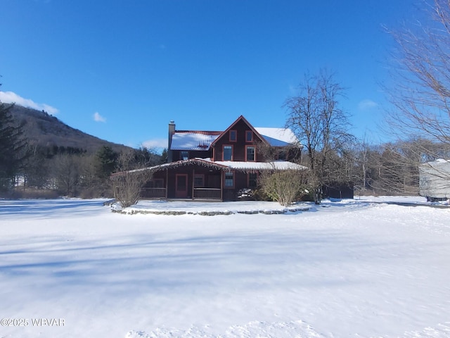 snow covered rear of property featuring covered porch