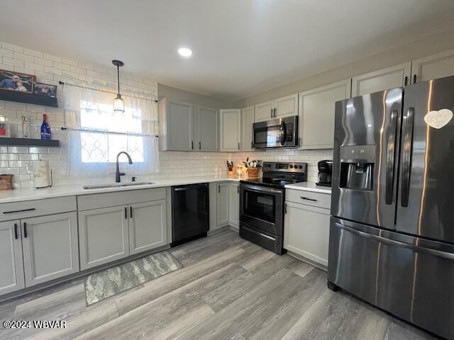 kitchen featuring tasteful backsplash, sink, black appliances, light hardwood / wood-style floors, and hanging light fixtures