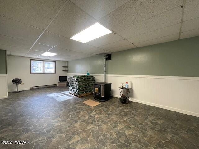 basement with a drop ceiling, a wood stove, and baseboard heating