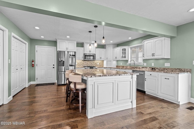 kitchen with stainless steel appliances, white cabinets, light stone countertops, a sink, and recessed lighting