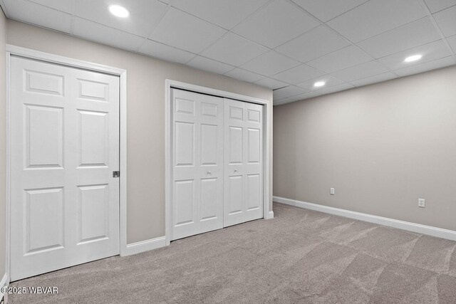 unfurnished bedroom with carpet, baseboards, recessed lighting, a closet, and a drop ceiling