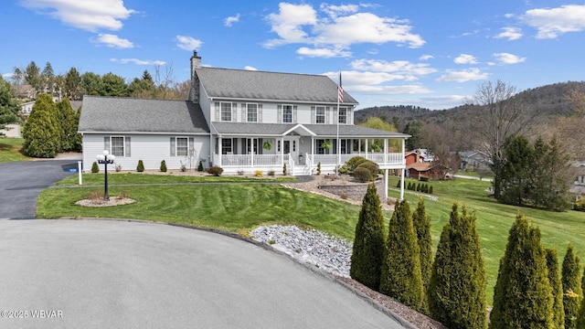 view of front of property featuring a porch, a front lawn, a chimney, and a shingled roof