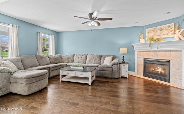 living room with dark wood-type flooring, a ceiling fan, and a fireplace