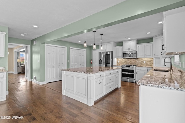 kitchen with stainless steel appliances, a sink, a kitchen island, dark wood-style flooring, and light stone countertops