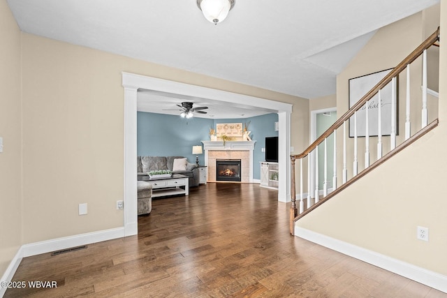 unfurnished living room with wood finished floors, ceiling fan, a tile fireplace, stairway, and baseboards