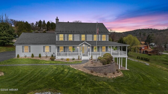 back of house at dusk with covered porch, a chimney, and a yard