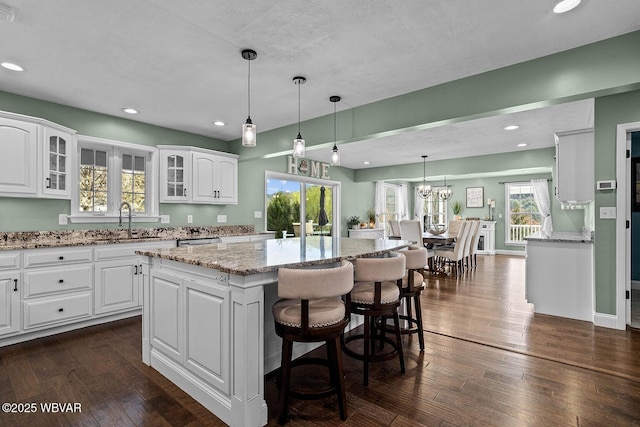 kitchen featuring a sink, glass insert cabinets, white cabinetry, a center island, and light stone countertops