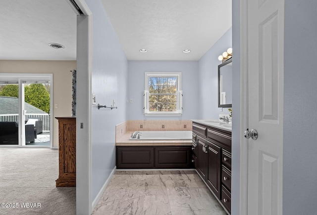 bathroom with plenty of natural light, a bath, marble look tiles, and vanity