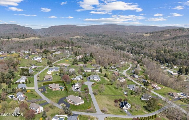 aerial view of property's location with a forest, a mountainous background, and nearby suburban area