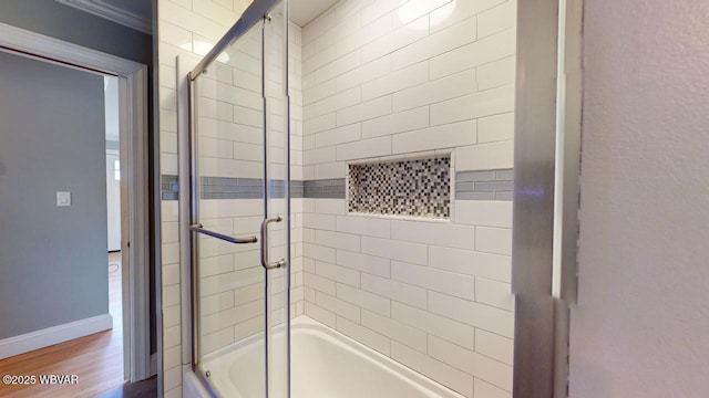 bathroom with hardwood / wood-style floors, bath / shower combo with glass door, and ornamental molding