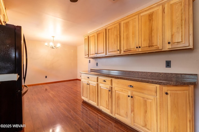 kitchen with light brown cabinets, hanging light fixtures, dark wood-type flooring, a chandelier, and black refrigerator