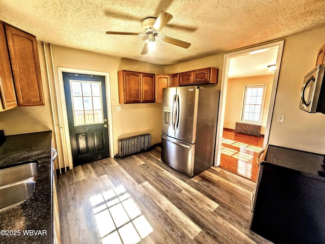 kitchen with wood finished floors, stainless steel appliances, radiator heating unit, a ceiling fan, and a textured ceiling