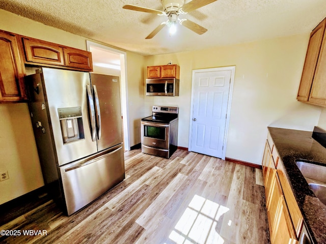 kitchen featuring stainless steel appliances, brown cabinets, ceiling fan, light wood finished floors, and a textured ceiling