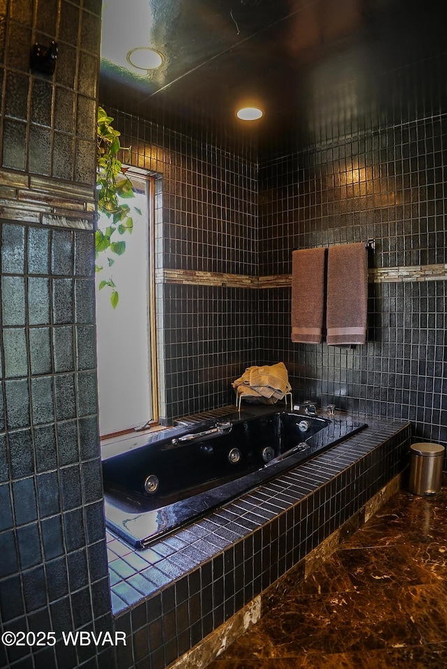 bathroom with marble finish floor, a jetted tub, and tile walls