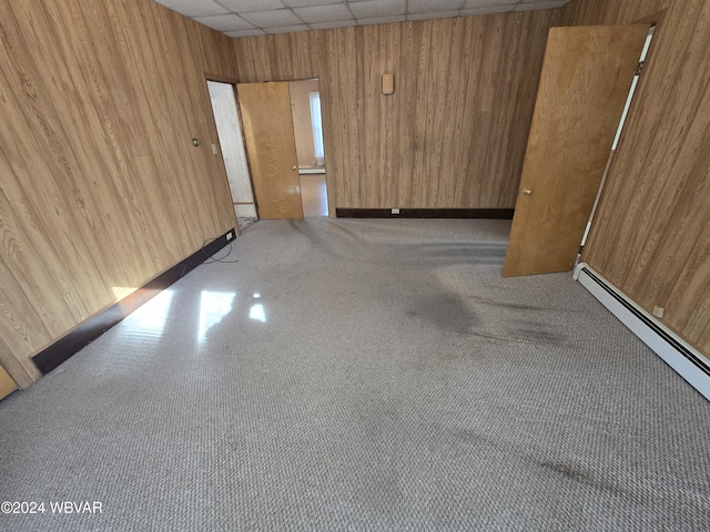 unfurnished room featuring a paneled ceiling, a baseboard radiator, and wooden walls