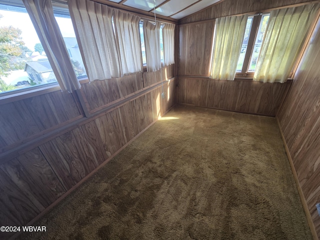 carpeted empty room with plenty of natural light, wood walls, and lofted ceiling