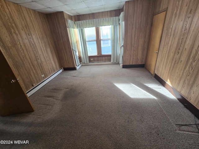 unfurnished room with a paneled ceiling, light colored carpet, wooden walls, and a baseboard radiator