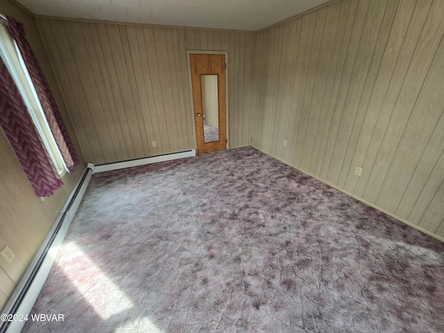 empty room featuring wood walls, carpet floors, and baseboard heating