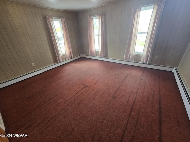 carpeted empty room featuring wood walls and a baseboard heating unit