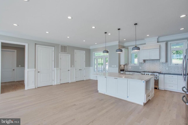 kitchen with tasteful backsplash, white cabinets, light wood-type flooring, a kitchen island with sink, and high end stove