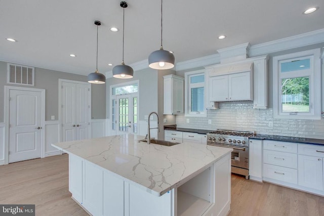 kitchen with decorative light fixtures, french doors, an island with sink, high end range, and sink