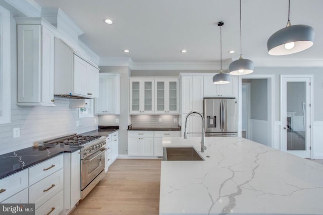 kitchen with appliances with stainless steel finishes, pendant lighting, tasteful backsplash, light hardwood / wood-style floors, and white cabinetry