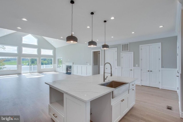 kitchen with an island with sink, light hardwood / wood-style flooring, white cabinetry, sink, and light stone counters