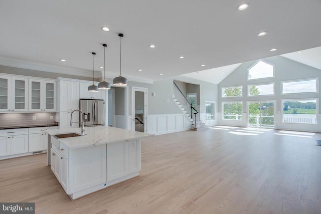 kitchen featuring decorative light fixtures, light stone counters, an island with sink, light wood-type flooring, and stainless steel fridge