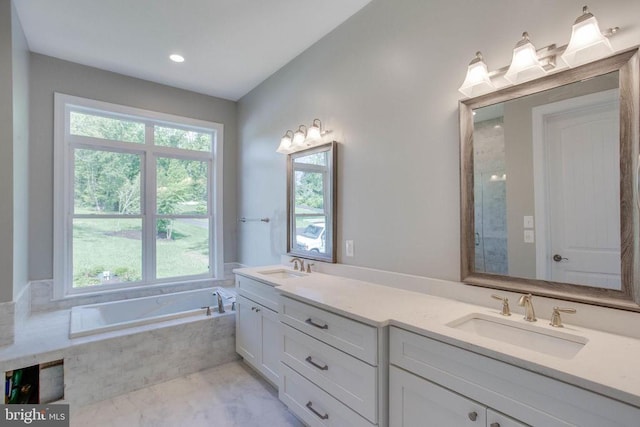 bathroom with a wealth of natural light, tiled bath, and dual bowl vanity