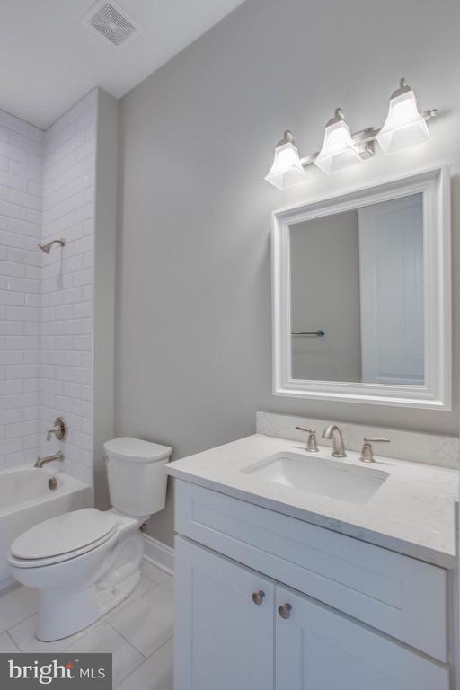 full bathroom with tiled shower / bath, toilet, tile floors, and vanity with extensive cabinet space