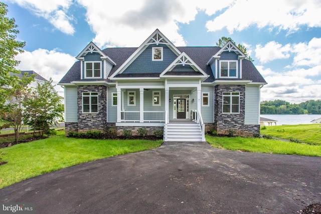 craftsman house with a front lawn, covered porch, and a water view