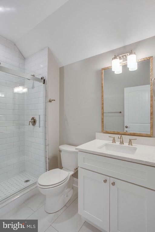 bathroom with tile flooring, lofted ceiling, tiled shower, toilet, and vanity