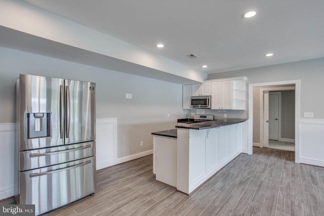 kitchen with appliances with stainless steel finishes, kitchen peninsula, light hardwood / wood-style floors, and white cabinets