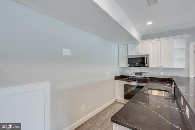 kitchen with appliances with stainless steel finishes, white cabinets, light hardwood / wood-style flooring, stainless steel counters, and sink