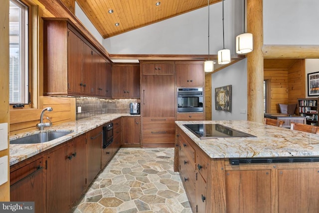 kitchen featuring oven, hanging light fixtures, black electric cooktop, sink, and light stone counters