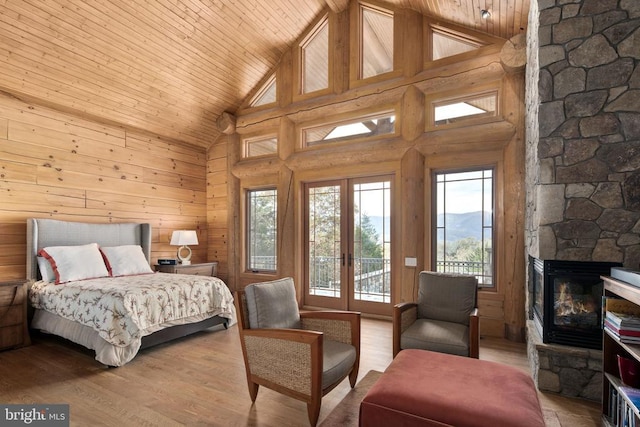 bedroom featuring wooden ceiling, wood walls, a stone fireplace, light hardwood / wood-style flooring, and high vaulted ceiling