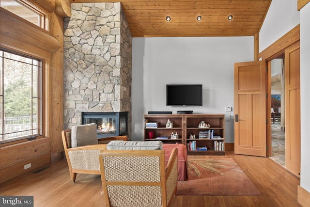 living room featuring high vaulted ceiling, light hardwood / wood-style flooring, wood ceiling, and a stone fireplace