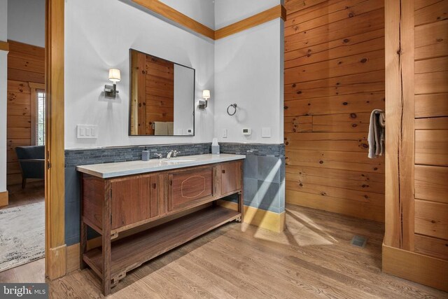 bathroom featuring vanity, wooden walls, wood-type flooring, and tasteful backsplash