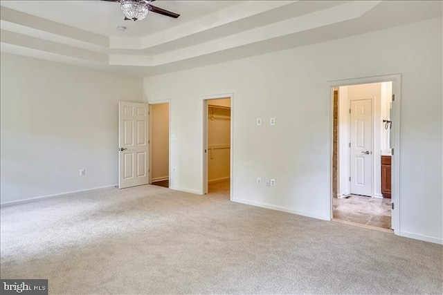 interior space featuring a walk in closet, light colored carpet, ceiling fan, and a tray ceiling