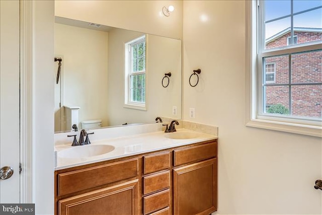 bathroom with toilet, double vanity, and a healthy amount of sunlight