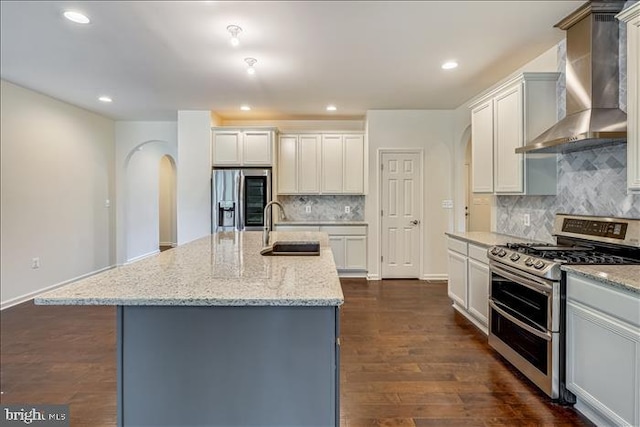 kitchen featuring an island with sink, sink, dark hardwood / wood-style flooring, stainless steel appliances, and wall chimney range hood