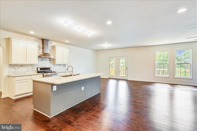 kitchen featuring stainless steel gas stove, dark hardwood / wood-style floors, a kitchen island with sink, wall chimney range hood, and sink