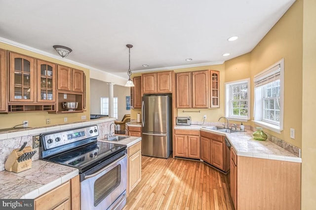 kitchen with appliances with stainless steel finishes, decorative light fixtures, light hardwood / wood-style floors, and sink