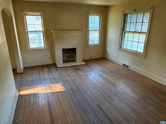 unfurnished living room with a wealth of natural light, a brick fireplace, and dark hardwood / wood-style floors