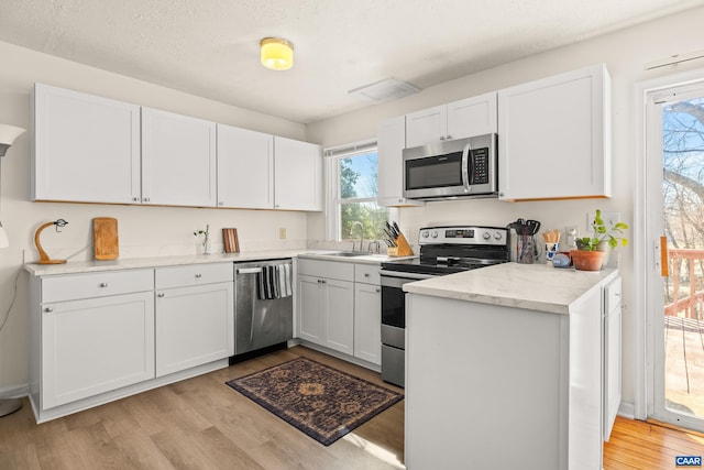 kitchen featuring white cabinetry, light wood finished floors, appliances with stainless steel finishes, and a sink