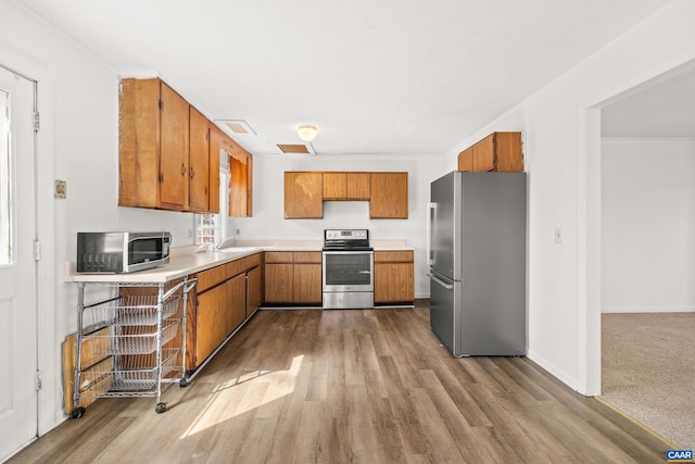 kitchen with light countertops, wood finished floors, brown cabinetry, and appliances with stainless steel finishes