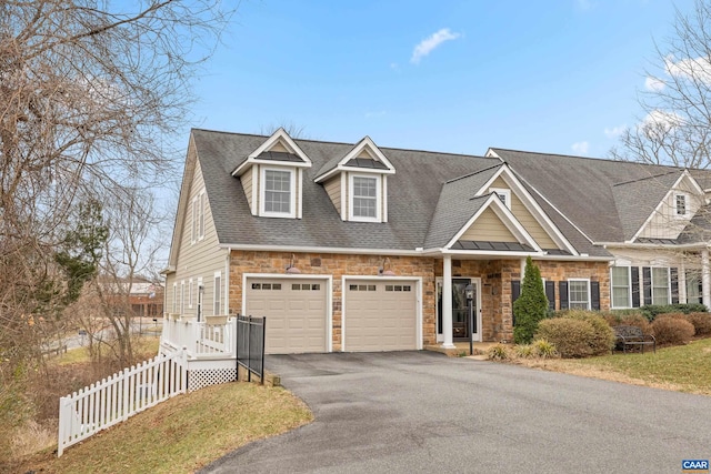 view of front facade with stone siding, driveway, a shingled roof, and fence